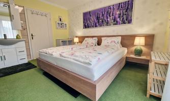 A cozy bedroom with a double bed and floral bedding. The walls are painted yellow and a soothing picture of lavender hangs above.