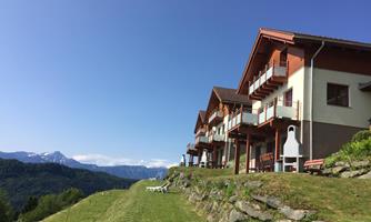 A building in the mountains with several balconies. The landscape is green and offers a view of the surrounding mountains.