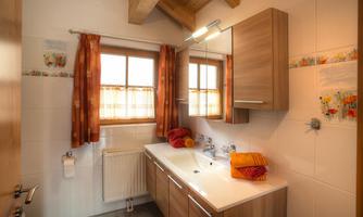 A modern bathroom with a wooden ceiling and large windows. Towels in warm colors are placed under the sink.