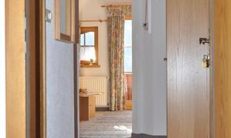 A bright hallway with a colorful runner and a half-open door. In the background, windows and a cozy living atmosphere are visible.