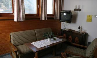 A cozy living space with two sofas and a table. Wooden paneling and windows with curtains can be seen on the walls.