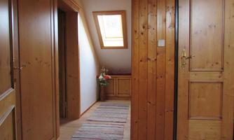 A bright corridor with wood paneling and a skylight. A colorful rug is on the floor, and to the right is a door.