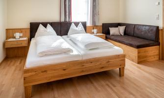A modern room with a double bed and a cozy seating area. The furnishings are made of wood and the walls are painted light.