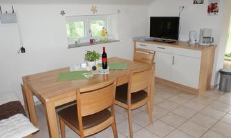 A cozy kitchen with a wooden dining area. On the table, there is a bottle of wine and fresh plants.