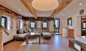 A cozy living room with a spacious couch and a wooden table. Bright walls and windows create an inviting atmosphere.