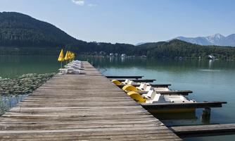 A tranquil lake with a wooden dock and yellow flags. Mountains are visible in the background.