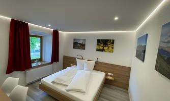 A modern bedroom with a double bed and two pillows. Red curtains and decorative pictures on the walls create a cozy atmosphere.