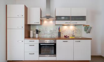 A modern kitchen with white cabinets and a wooden countertop. The equipment includes a stove, a hood, and various kitchen utensils.