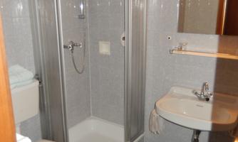 A small bathroom with a modern shower, sink, and toilet. The walls are tiled with gray tiles, and there is lighting above the mirror.