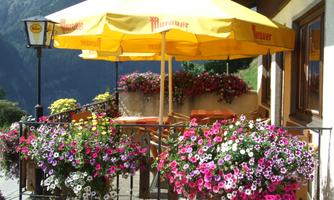 A cozy terrace with a yellow sun umbrella and blooming flowers. The surroundings are green and invite relaxation.