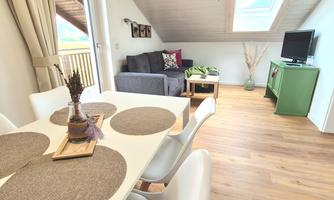 A modern living room with a dining table and a sofa. Bright colors and large windows create a pleasant atmosphere.