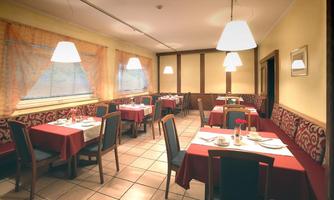 A cozy restaurant with red tablecloths and elegant lamps.  
The tables are nicely set and there are large windows with curtains.