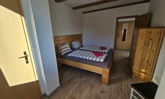 A simple bedroom with two beds and wooden elements. The room has a warm, cozy feel.