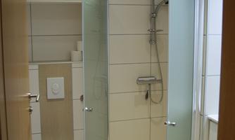 A modern bathroom with a shower and a toilet. The walls are tiled in light colors and fresh towels are ready.