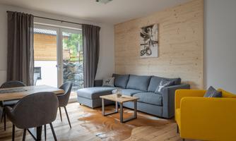 A modern living room with a gray sofa and a yellow armchair. Large windows provide plenty of daylight and a view outside.