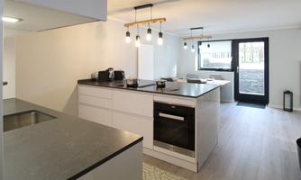 A modern kitchen with a large kitchen island and elegant pendant lights. The space is bright and open, with access to an outdoor area.