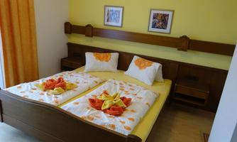 A cozy bedroom with a double bed and bright walls. The bed linen is decorated with colorful towels and there are small pictures on the wall.