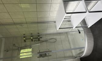 A modern bathroom with a transparent shower cubicle and white tiles. Next to the shower stands a practical three-tier shelf.