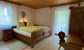 A cozy bedroom with wooden ceilings and a large bed. There is a desk and plenty of daylight through the windows.