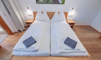 A bright, modern bedroom with two single beds and clean bed linen. The warm wood paneling and soft lighting create an inviting atmosphere.