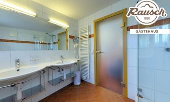 A bright bathroom with modern fixtures and large mirrors. The walls are tiled in white, and the door is made of frosted glass.