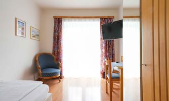 A bright room with a window that lets in plenty of light. There is a cozy armchair, a table, and a television.