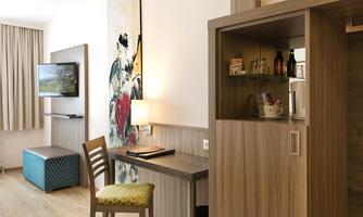 A modern room with a desk, a television, and a small refrigerator. The walls are bright and adorned with decorative elements.