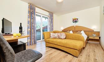 A modern room with a yellow sofa, a table, and a television. The room has large windows and is bright and welcoming.