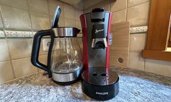 A modern coffee machine in red by Philips stands next to a glass coffee pot on a gray countertop. The surroundings feel cozy and inviting.
