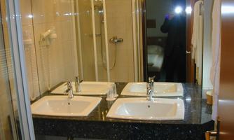 A modern bathroom with two sinks on a dark marble surface. In the background, a shower and a towel are visible.