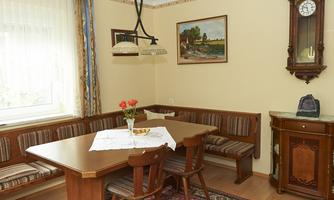 A cozy dining area with a wooden table and benches. A painting hangs on the wall, and a wall-mounted clock gives the room a classic charm.