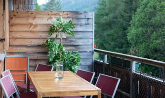 A cozy balcony with a wooden table and chairs. In the background, trees and a natural landscape can be seen.