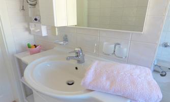 A modern bathroom with a sink and a large mirror. A pink towel lies next to the sink on a white shelf.
