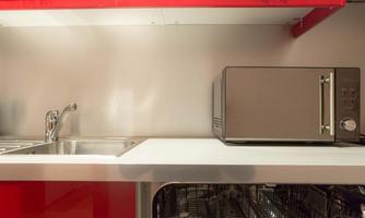A modern kitchen with a stainless steel sink and a microwave. The walls and shelves are designed in red and silver.