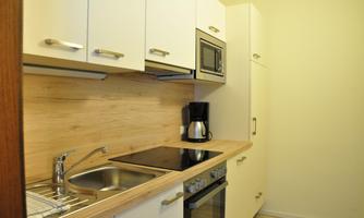 A modern kitchen with light cabinets and wooden details. It is equipped with a stove, a microwave, and a coffee maker.