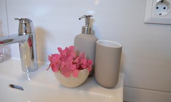 A modern bathroom with a shiny faucet, a soap dispenser bottle, and a cup. There is a decorative bowl with pink flowers.