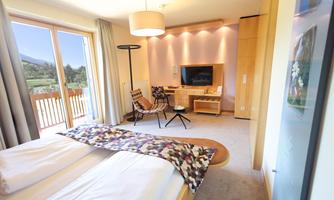 A modern room with a large window and a view of nature. The decor is bright and friendly, featuring a comfortable bed and a cozy seating area.