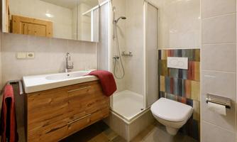 A modern bathroom with a shower and a wooden sink cabinet. The walls are light-tiled, and colorful accents create a cheerful look.