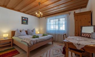 A cozy bedroom with two beds, a wooden ceiling, and a window alcove. A mirror is on the table, and decorative elements create an inviting atmosphere.