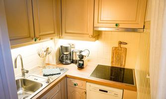 A small kitchen with beige cabinets and a modern cooktop. The room is brightly lit and contains appliances like a coffee machine and a dishwasher.
