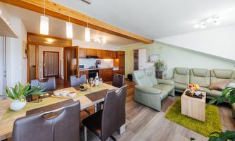 A modern apartment with an open living kitchen and a cozy living room. The space is bright and inviting with a dining table and comfortable armchairs.