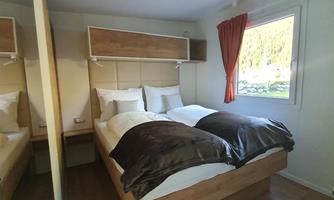 A stylish bedroom with two beds and cozy bedding. Natural light streams through the window, and there is a modern wooden wardrobe.