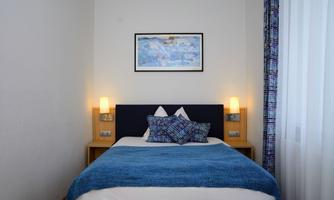 A cozy bedroom with a double bed and blue accents. There are two nightstands with lamps and a picture on the wall.