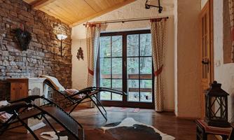 A cozy room with wooden walls and large windows overlooking a green outdoor area. Relaxation chairs and an animal fur mat give the environment a rustic atmosphere.