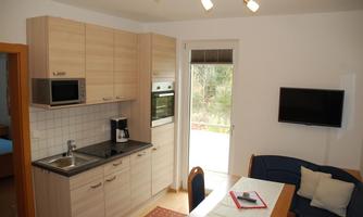 A modern kitchen with wooden cabinets and modern appliances. The dining area is bright and cozy, with a blue couch and a table.
