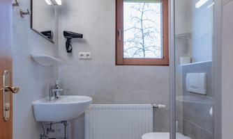 A modern bathroom with gray tiles and a window. It includes a sink, a shower, and a radiator.