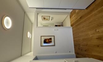 A bright hallway with white wall design and wooden flooring. A picture hangs on the wall, and a door leads to another room.