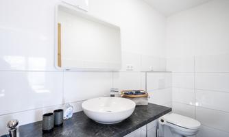 A modern bathroom with white tiles and an elegant sink. There is a large mirror and a stylish toilet.