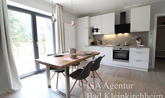 A modern kitchen with a wooden dining area and elegant chairs. Large windows let in plenty of light and offer a view of the outdoors.