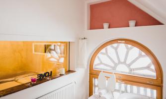 A bright room with a large, round window and a cozy seating area. The walls are painted in soft colors and there are decorative elements.